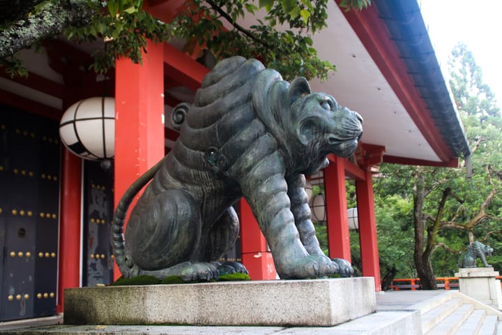 front of the temple, with a copper or bronze statue of a cat arching its back, thumbnail